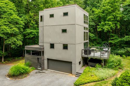 Aerial view of a tall modern home with an elevated deck surrounded by dense woodland