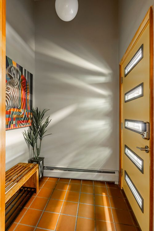 Entry foyer with terracotta tile floor, a wood bench, colorful zebra artwork and glass-paneled door