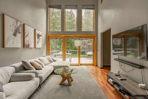Two-story living room with floor-to-ceiling windows, a gray sectional and round glass coffee table