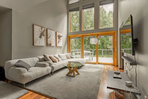 Living room with tall wood-framed windows overlooking trees and a gray sectional sofa