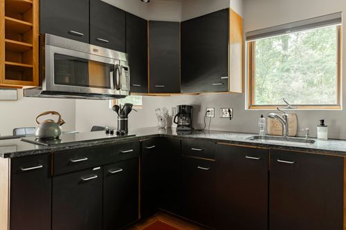 Sleek black kitchen cabinetry with a stainless microwave and dark granite countertops