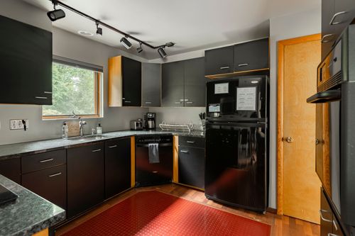 Black kitchen with black appliances, a red patterned floor mat and mustard yellow door
