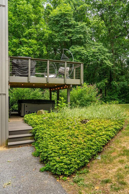 Elevated wood deck with cable railings and a hanging egg chair over a hot tub patio