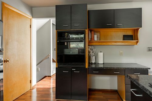 Built-in black cabinetry with wall ovens and an open wood shelf display niche