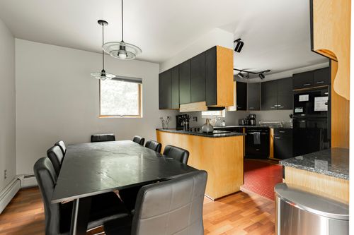 Dining table with black leather chairs under globe pendant lights, kitchen visible beyond