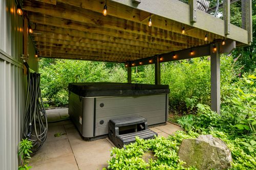 Covered patio with a hot tub and step stool beneath a string-lit deck