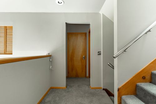 Upstairs landing with a wood door, carpeted floor and staircase railing