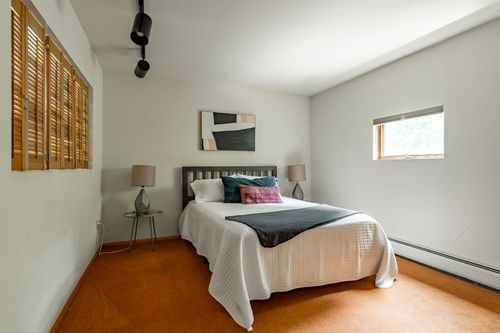 Bedroom with a gray upholstered headboard, plantation shutters and orange carpet