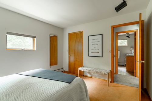 Bedroom with a white bed and framed art beside a doorway open to an ensuite bathroom