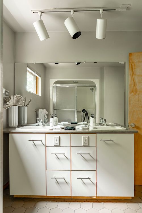 Double-sink bathroom vanity with a large mirror and white cabinetry under track lighting