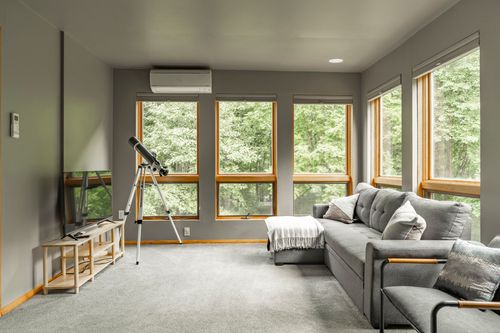 Bright loft room with tall windows, wall-mounted heat pump and a gray sectional sofa