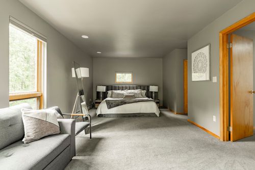 Primary bedroom with a dark upholstered bed and reading chair on plush gray carpet