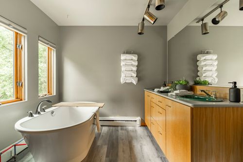 Primary bathroom with a freestanding soaking tub, woven towel rack and wood vanity with green sinks