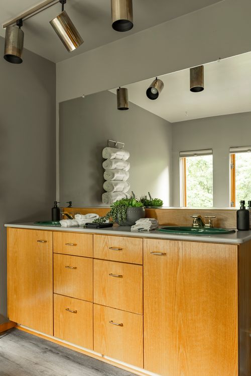 Primary bathroom vanity with wood cabinetry and a large mirror reflecting the soaking tub