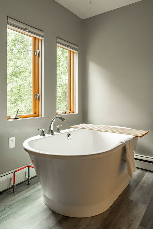 Freestanding white soaking tub positioned beneath two tall windows