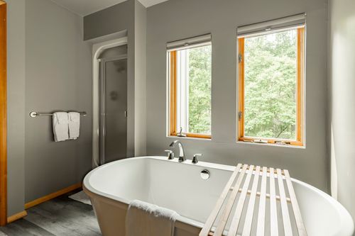 Bathroom with a corner glass shower and a freestanding tub near two shaded windows