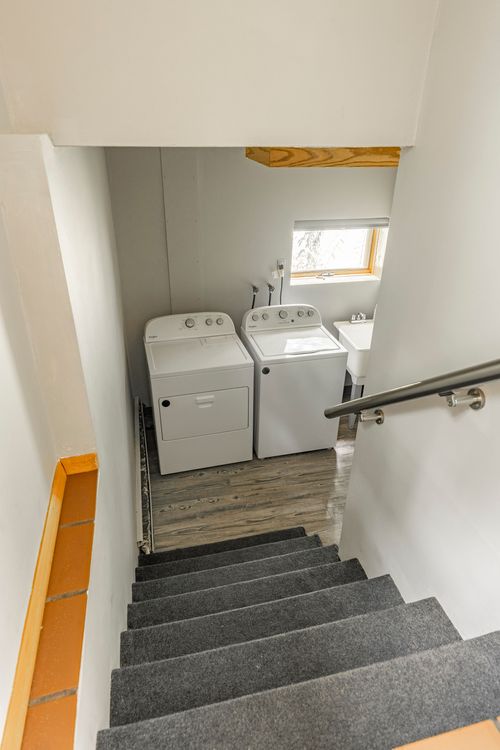 View down a staircase to a laundry room with a washer, dryer and wood trim