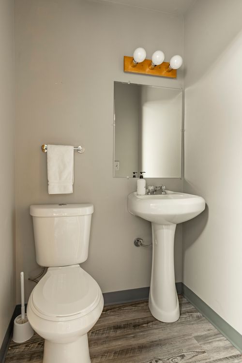 Powder room with a pedestal sink, wood-topped vanity light and framed mirror