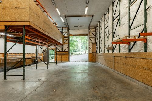 Barn interior near an open bay door with a view of the surrounding woods
