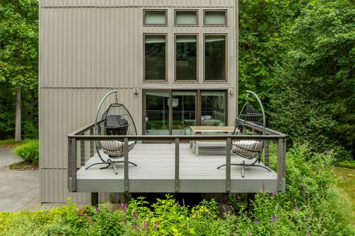 Rear elevation of a modern gray tower home with an elevated deck and egg chairs