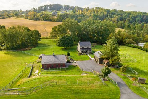 Aerial view of a stone farmhouse, red barn and outbuildings surrounded by rolling pasture and woods