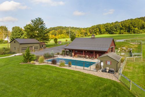Aerial view of a red barn, pool and garage building beside a winding driveway and green lawn