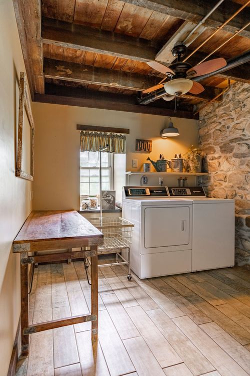 Laundry room with stone accent wall, wood-beam ceiling and wooden folding table