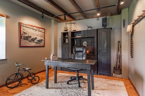 Rustic home office with black desk, exposed ceiling beams and antique tricycle