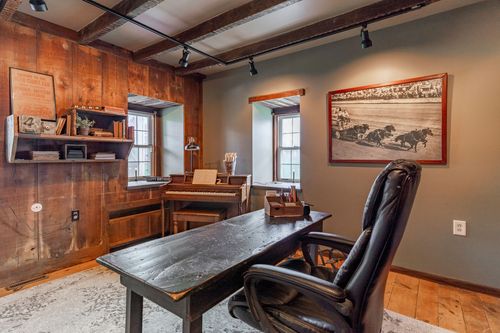 Wood-paneled home office with leather desk chair, upright piano and framed horse print