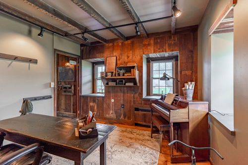 Rustic wood-paneled office with upright piano and exposed metal ceiling beams