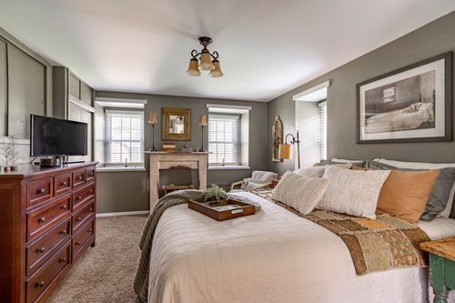 Neutral bedroom with wood dresser, fireplace mantel and layered throw pillows