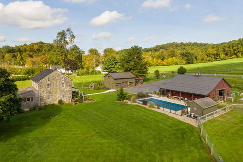 Aerial view of a stone farmhouse, pool and outbuildings with rolling farmland in the distance