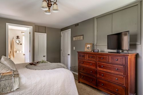 Bedroom with cherry wood dresser, wall-mounted TV and doorway to a bathroom