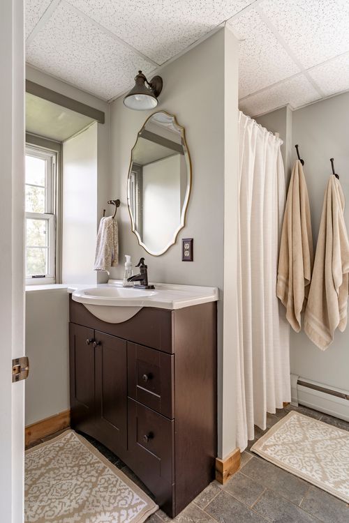Bathroom with dark wood vanity, oval mirror and towels hanging by the shower