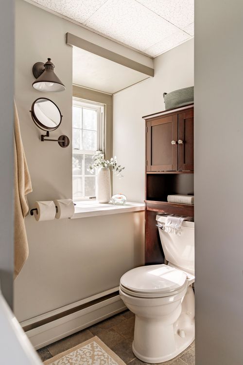 Half bath with wood over-toilet cabinet, window ledge vase and towel hooks