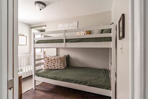 Kids room with white bunk beds, green bedding and a dinosaur-print pillow