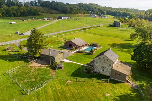 Aerial view of two stone farmhouses and a red barn set among fields, sheds and farm equipment