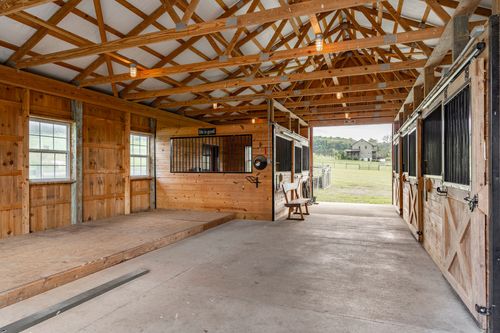 Barn interior with exposed wood trusses, horse stall and open sliding door to pasture