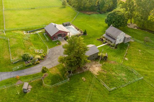 Aerial view of a red barn and stone house connected by driveways amid fenced green pasture