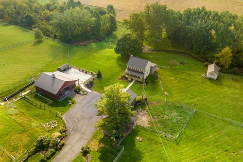 Aerial view of a stone farmhouse with a pool and small outbuilding surrounded by open fields