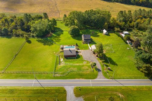 Aerial view of a stone farmhouse with a pool along a country road bordered by golden farmland