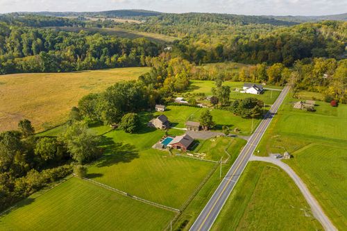 Aerial view of a stone farmhouse with a pool sitting beside a country road amid rolling fields