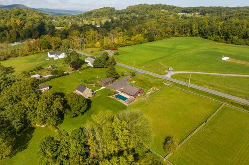Aerial view of a stone farmhouse, pool and barn set among fenced fields near distant mountains