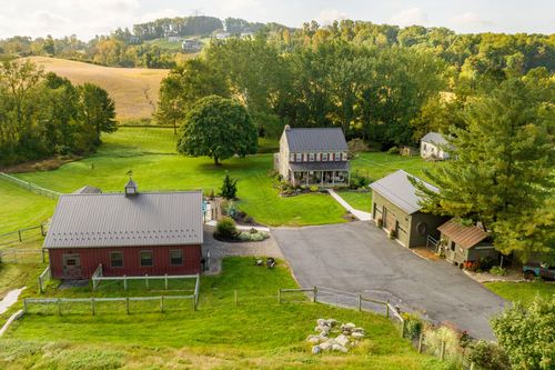 Aerial view of a stone farmhouse, red bank barn and driveway framed by rolling hills and trees