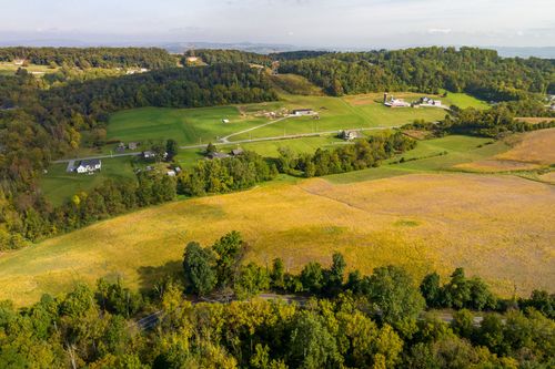Aerial view of farm buildings and pasture nestled among wooded hills and winding roads