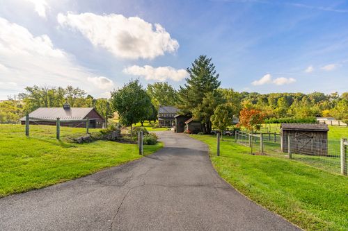 Driveway leading past a red barn to a stone farmhouse framed by mature trees