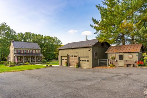 Exterior of a detached garage and stone farmhouse beside a paved driveway and lawn