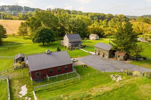 Aerial view of a red barn, stone farmhouse and garage building set on a green rural property