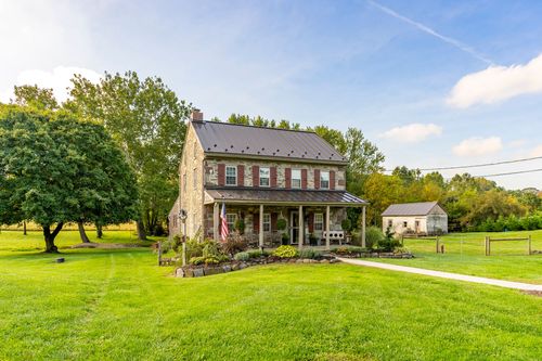 Stone farmhouse exterior with a metal roof, covered porch, American flag and manicured landscaping
