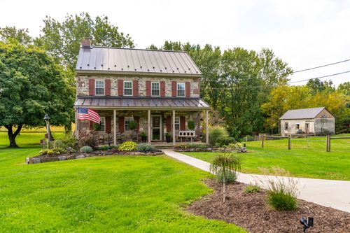 Stone farmhouse with a covered porch, American flag and stone walkway through landscaped beds